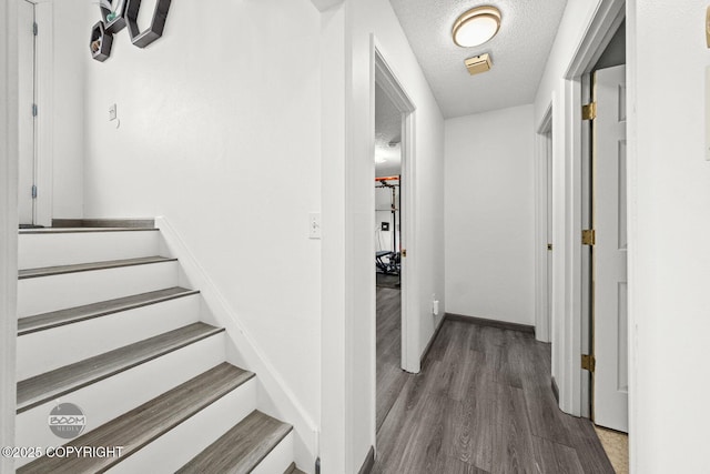 corridor with baseboards, wood finished floors, a textured ceiling, and stairs