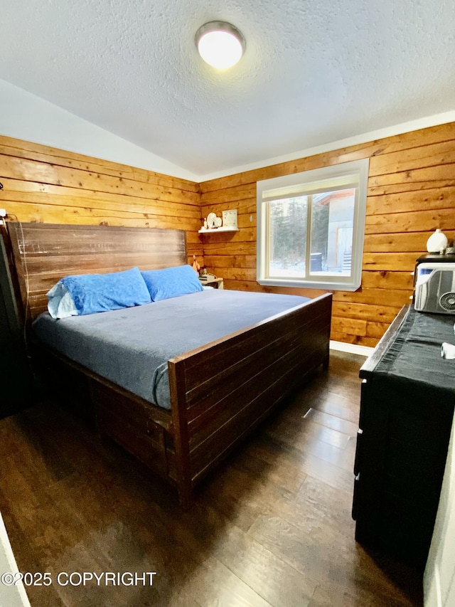 bedroom with lofted ceiling, dark wood-type flooring, a textured ceiling, and wood walls