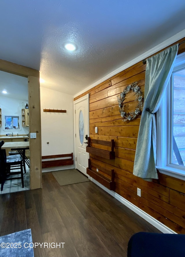 entryway with dark wood-type flooring, a textured ceiling, and wood walls