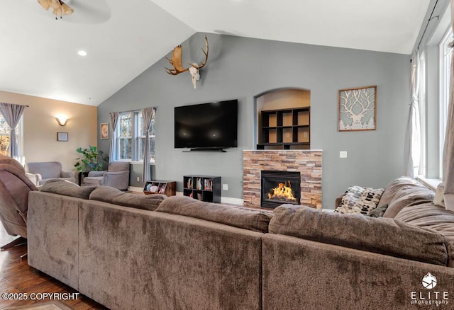 living room with dark hardwood / wood-style flooring, a stone fireplace, a wealth of natural light, and lofted ceiling