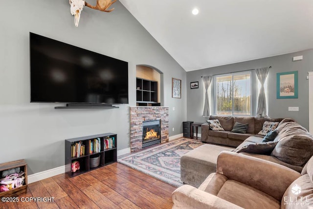 living room with hardwood / wood-style floors, a stone fireplace, and high vaulted ceiling