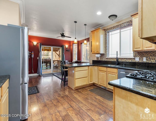 kitchen featuring appliances with stainless steel finishes, light brown cabinetry, decorative light fixtures, sink, and kitchen peninsula