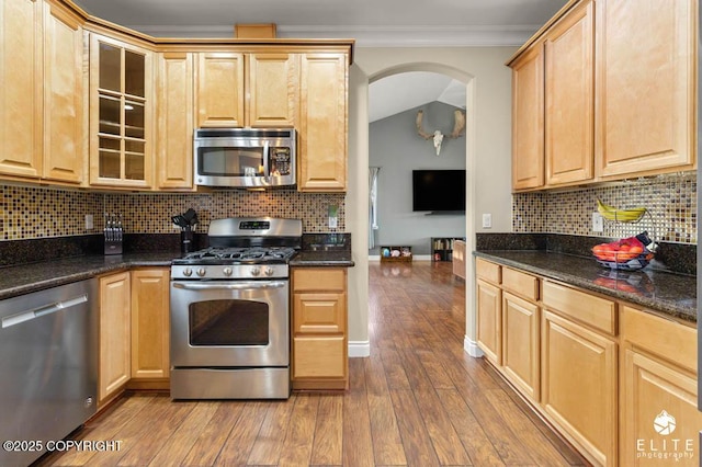 kitchen featuring crown molding, dark stone countertops, stainless steel appliances, wood-type flooring, and decorative backsplash