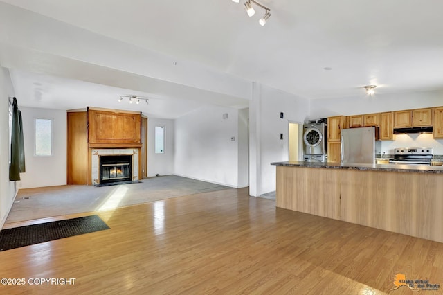 kitchen with appliances with stainless steel finishes, stacked washer and dryer, light wood-type flooring, and under cabinet range hood