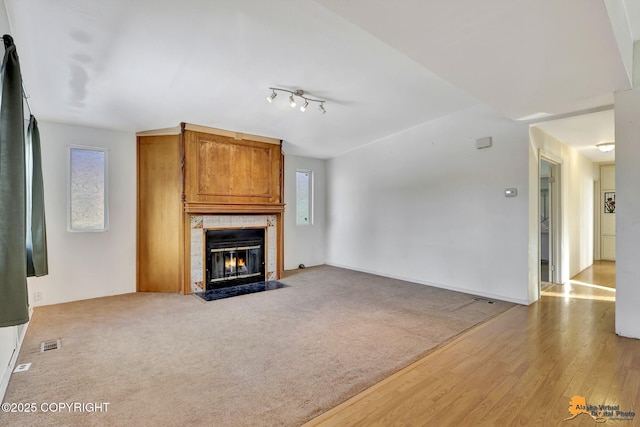 unfurnished living room featuring a large fireplace, carpet, visible vents, and wood finished floors