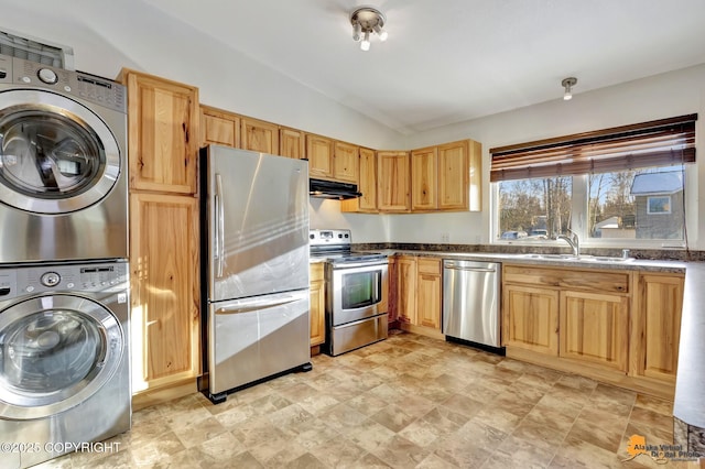 kitchen featuring lofted ceiling, under cabinet range hood, stacked washer / dryer, a sink, and appliances with stainless steel finishes