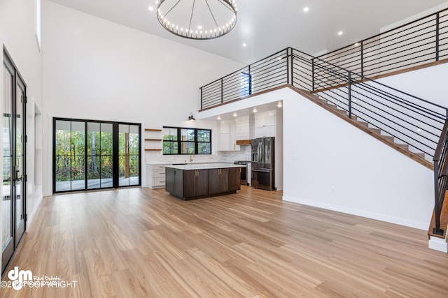 unfurnished living room with a high ceiling, a notable chandelier, and light hardwood / wood-style floors