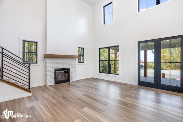 unfurnished living room featuring a fireplace, a wealth of natural light, light hardwood / wood-style flooring, and a towering ceiling