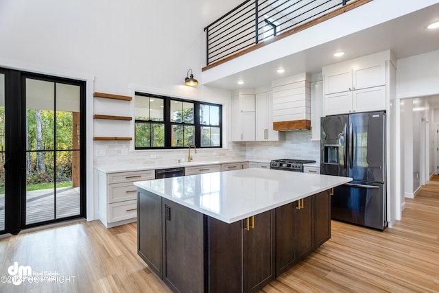 kitchen featuring white cabinets, a center island, dark brown cabinetry, black appliances, and light wood-type flooring