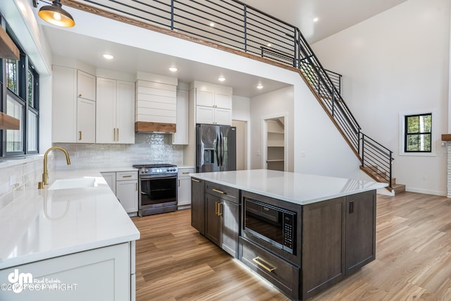 kitchen with built in microwave, white cabinetry, a center island, black refrigerator with ice dispenser, and stainless steel range with gas cooktop