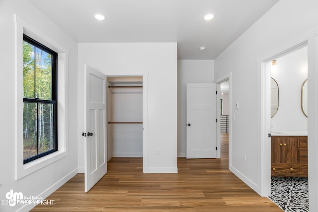 unfurnished bedroom featuring a walk in closet, ensuite bathroom, a closet, and light hardwood / wood-style flooring