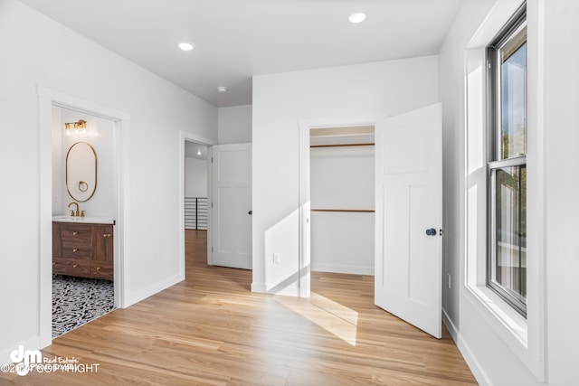 unfurnished bedroom featuring sink, ensuite bath, a spacious closet, a closet, and light wood-type flooring