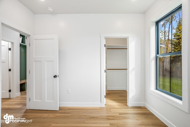 unfurnished bedroom with multiple windows, a walk in closet, a closet, and light wood-type flooring