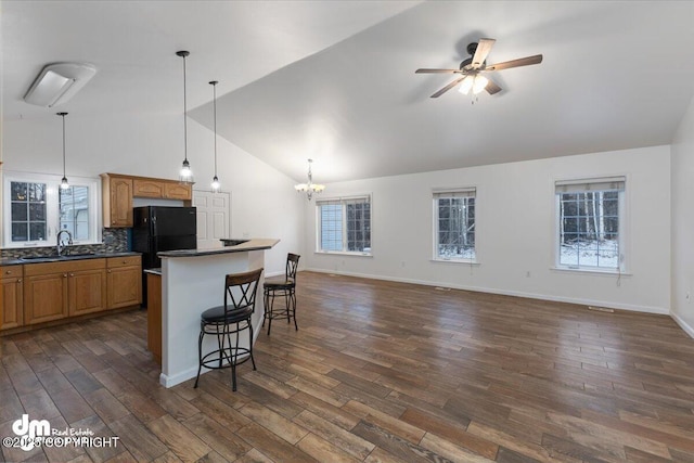 kitchen featuring sink, dark wood-type flooring, black refrigerator, a kitchen bar, and ceiling fan with notable chandelier