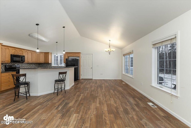 kitchen featuring decorative light fixtures, a breakfast bar area, black appliances, and dark hardwood / wood-style floors