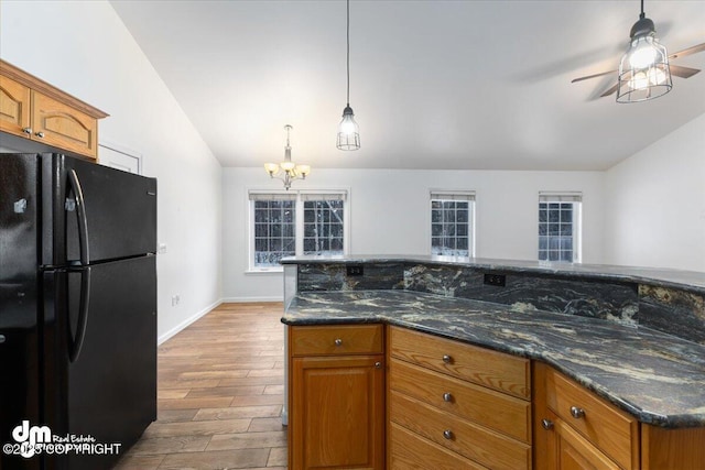 kitchen with decorative light fixtures, vaulted ceiling, light hardwood / wood-style flooring, black refrigerator, and ceiling fan with notable chandelier