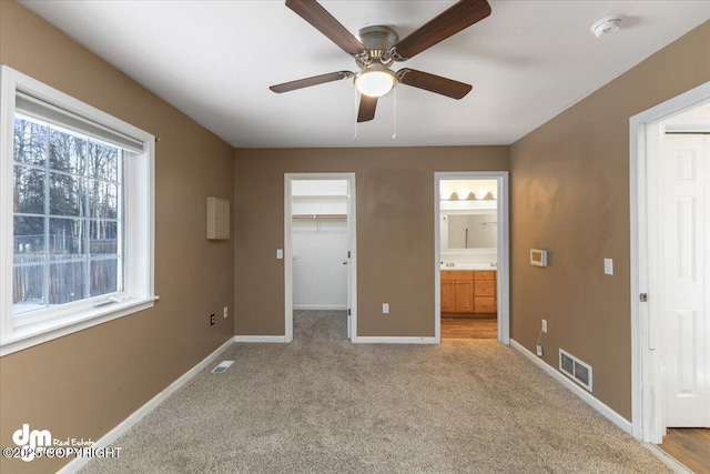 unfurnished bedroom featuring connected bathroom, a walk in closet, light colored carpet, a closet, and ceiling fan