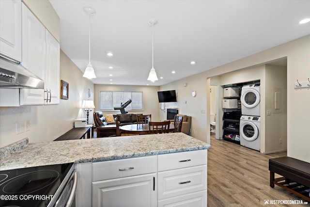 kitchen with white cabinetry, stacked washer / dryer, decorative light fixtures, and light hardwood / wood-style floors