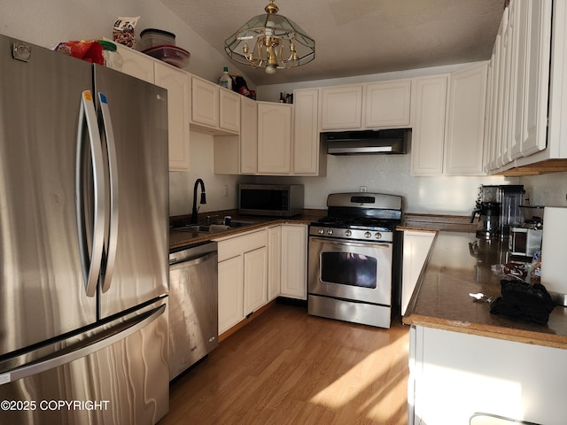 kitchen with appliances with stainless steel finishes, decorative light fixtures, white cabinetry, sink, and hardwood / wood-style flooring