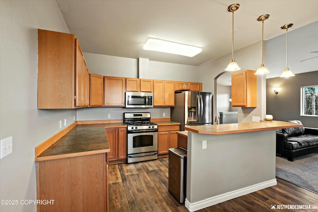 kitchen featuring pendant lighting, dark wood finished floors, a breakfast bar area, appliances with stainless steel finishes, and a peninsula