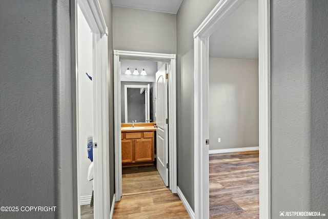 hallway with a sink, baseboards, and wood finished floors