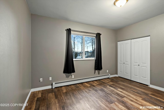 unfurnished bedroom with a closet, baseboards, baseboard heating, and dark wood-type flooring