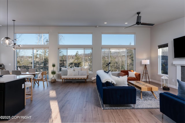 living room featuring wood-type flooring, ceiling fan with notable chandelier, and a high ceiling