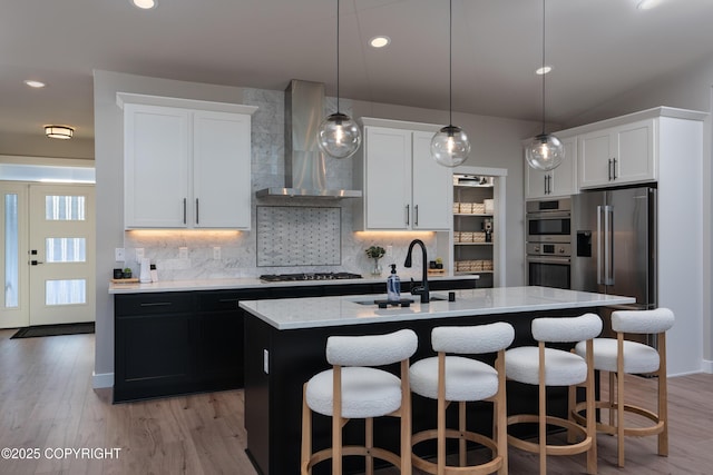 kitchen featuring white cabinetry, decorative light fixtures, a kitchen island with sink, and wall chimney range hood