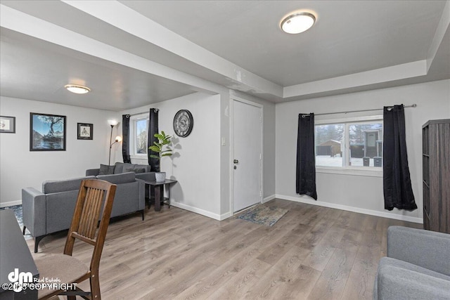 living room with a tray ceiling, a wealth of natural light, and light wood-type flooring