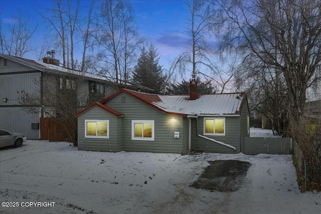 snow covered house with a chimney, metal roof, and fence