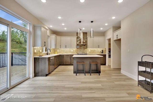 kitchen with pendant lighting, wall chimney range hood, sink, a center island, and tasteful backsplash