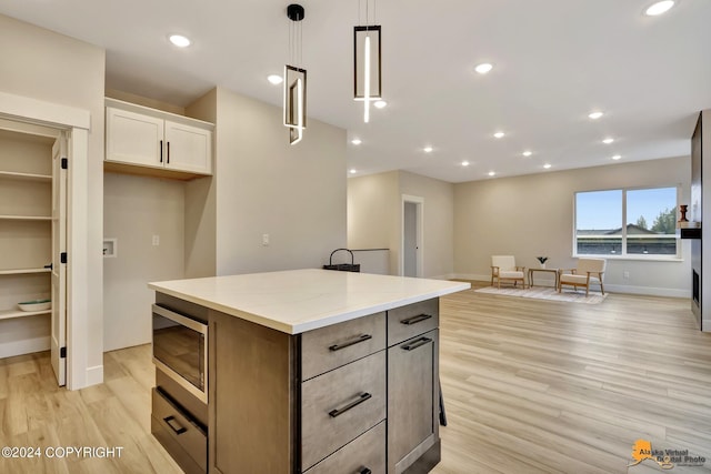 kitchen featuring a kitchen island, stainless steel microwave, white cabinets, light stone counters, and light hardwood / wood-style floors