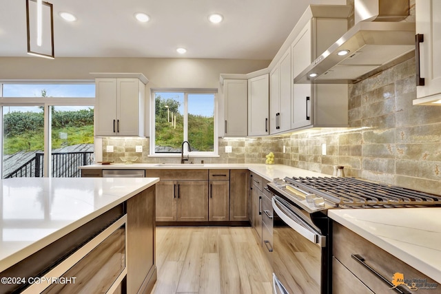 kitchen with wall chimney range hood, sink, white cabinets, and appliances with stainless steel finishes