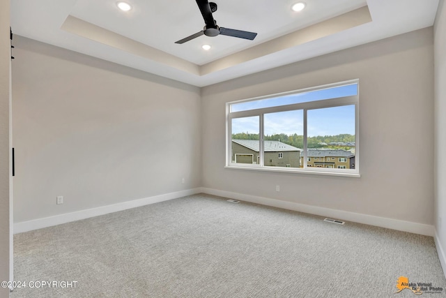 carpeted spare room with ceiling fan and a raised ceiling