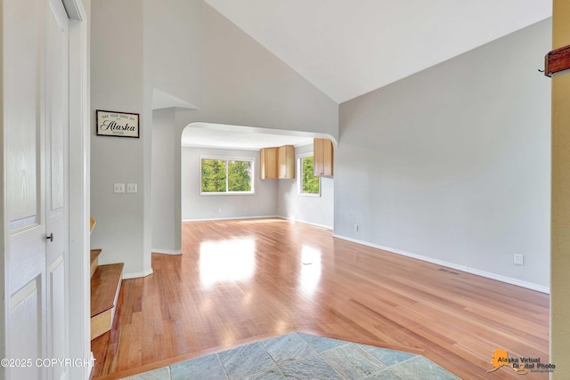 10235 Stewart Dr, Eagle River, AK 99577 - unfurnished living room featuring arched walkways, high vaulted ceiling, wood finished floors, and stairs