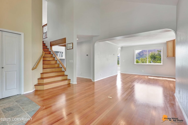 10235 Stewart Dr, Eagle River, AK 99577 - unfurnished living room featuring arched walkways, light wood-type flooring, a high ceiling, and stairs