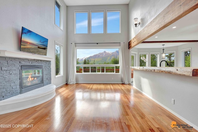 10235 Stewart Dr, Eagle River, AK 99577 - unfurnished living room featuring a stone fireplace, light wood finished floors, beam ceiling, a towering ceiling, and recessed lighting