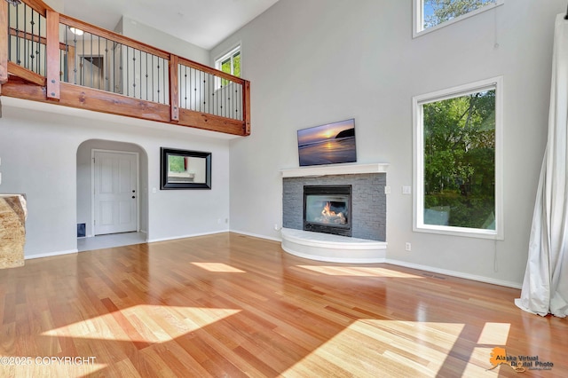 10235 Stewart Dr, Eagle River, AK 99577 - unfurnished living room featuring a high ceiling, a glass covered fireplace, wood finished floors, plenty of natural light, and arched walkways