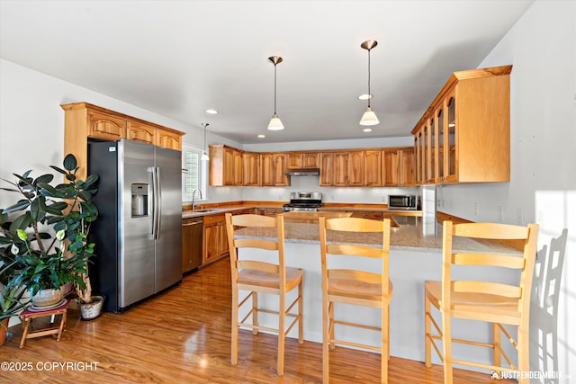 kitchen featuring sink, light wood-type flooring, a kitchen breakfast bar, stainless steel appliances, and light stone countertops