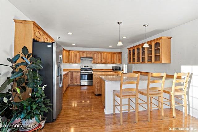 kitchen featuring a breakfast bar, light stone counters, a center island, light hardwood / wood-style flooring, and appliances with stainless steel finishes