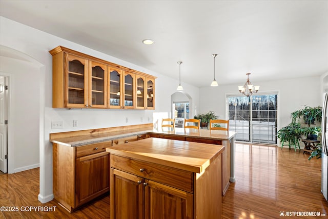 kitchen with pendant lighting, a center island, light stone counters, an inviting chandelier, and light hardwood / wood-style flooring