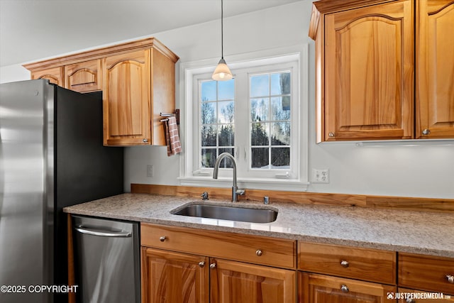 kitchen featuring stainless steel refrigerator, light stone counters, sink, and hanging light fixtures