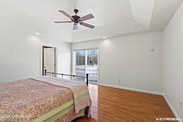 bedroom featuring a raised ceiling, hardwood / wood-style flooring, access to exterior, and ceiling fan