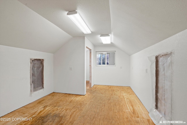 additional living space with vaulted ceiling, hardwood / wood-style floors, and a textured ceiling