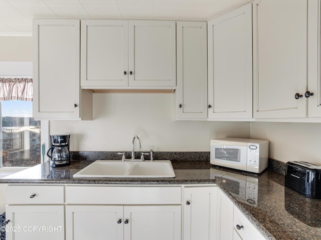kitchen featuring dark stone countertops, sink, and white cabinets