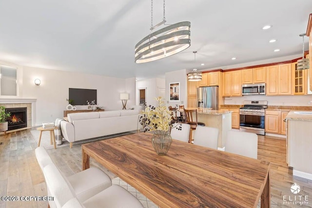 dining area featuring sink, a notable chandelier, a tile fireplace, and light wood-type flooring