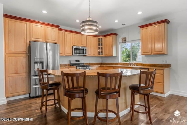 kitchen featuring appliances with stainless steel finishes, pendant lighting, dark hardwood / wood-style flooring, a center island, and light stone countertops