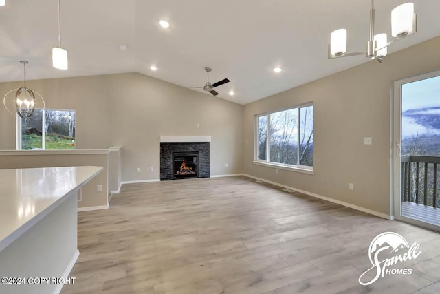 unfurnished living room with ceiling fan with notable chandelier, light hardwood / wood-style floors, and vaulted ceiling