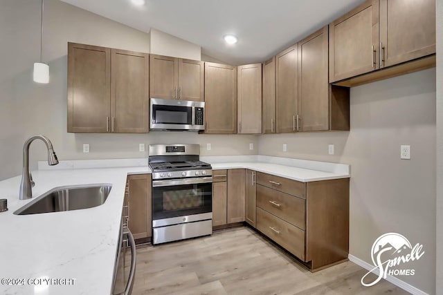 kitchen with lofted ceiling, sink, appliances with stainless steel finishes, hanging light fixtures, and light wood-type flooring