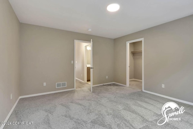 unfurnished bedroom with a walk in closet and light colored carpet